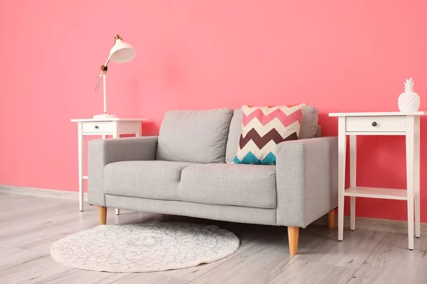 Comfortable sofa and modern lamp on table near pink wall