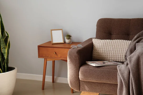 Comfortable armchair and stylish table near light wall