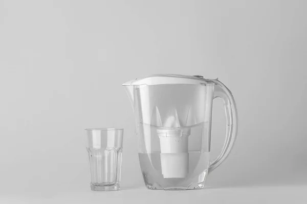 Filter jug and glass of water on grey background