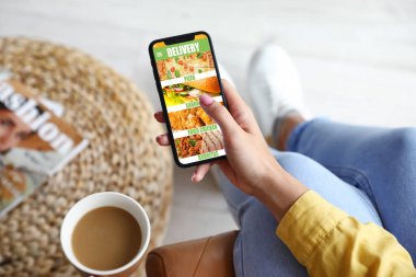 İnternetten yemek sipariş etmek için akıllı telefon kullanan genç bir kadın.
