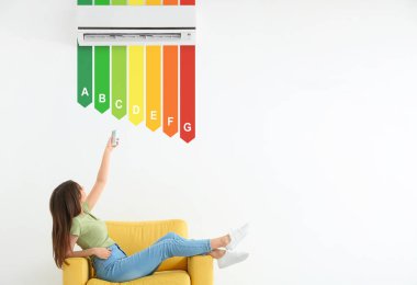 Genç bir kadın odasındaki modern klimayı açıyor. Akıllı ev kavramı