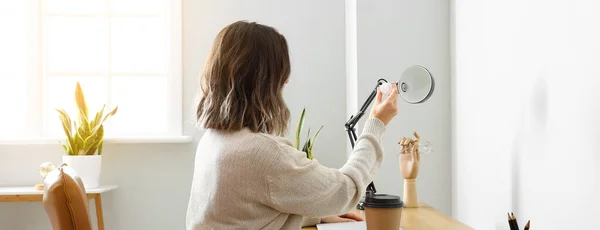 Woman changing light bulb of table lamp at workplace in office