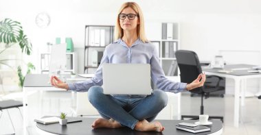 Bilgisayarlı güzel iş kadını ofiste meditasyon yapıyor.