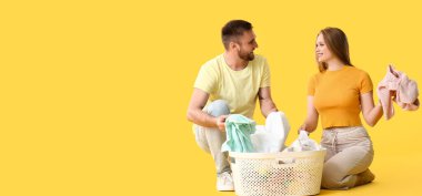 Sarı arka planda çamaşır sepetli genç çift mesaj için yer var.