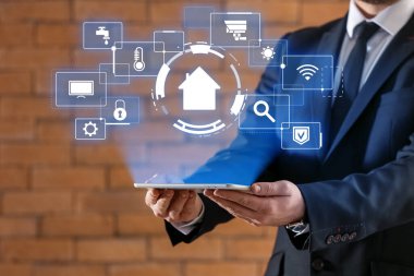 Tablet bilgisayarı olan bir adam tuğla arka planda akıllı ev otomasyonunun geleceksel arayüzünü kullanıyor