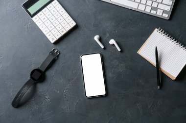Koyu arkaplanda cep telefonu, kol saati, kulaklık ve kırtasiye malzemesi olan kompozisyon