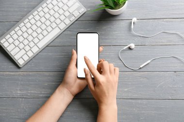 Gri ahşap arka planda cep telefonu, klavye ve kulaklık takan kadın elleri