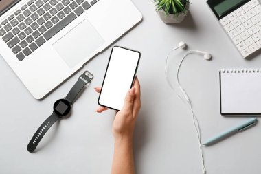 Beyaz arka planda cep telefonu, kol saati, kulaklık ve dizüstü bilgisayarı olan bir kadın.