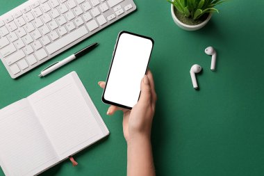 Renkli arka planda cep telefonu, defter, kulaklık, kalem ve klavye olan kadın eli