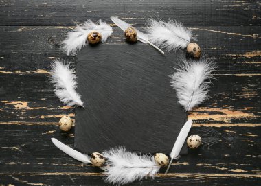 Güzel beyaz tüyleri, bıldırcın yumurtaları ve siyah ahşap arka planı olan kompozisyon.