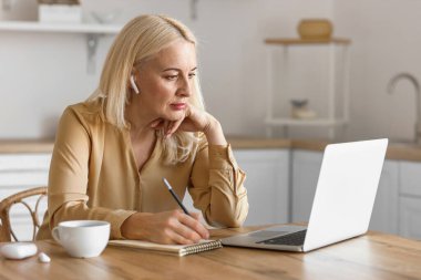 Mutfakta dizüstü bilgisayarı olan olgun bir kadının sabahı.