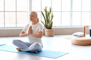 Olgun bir kadının evde meditasyon yaptığı bir sabah.