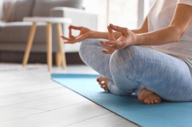 Olgun bir kadının evde meditasyon yaptığı bir sabah.