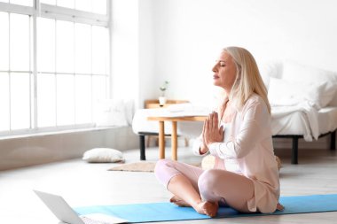 Olgun bir kadının evde meditasyon yaptığı bir sabah.
