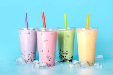 Farklı arkaplanda farklı lezzetli köpüklü çay ve buz küplerinden plastik bardaklar.