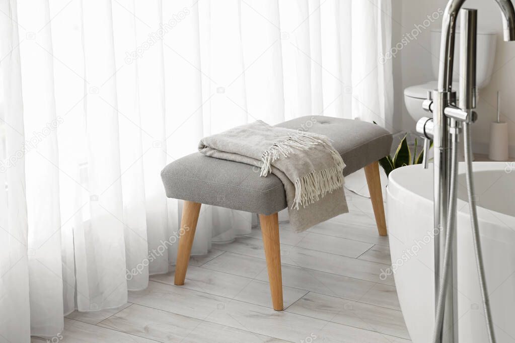 Soft bench with plaid near light curtain in bathroom