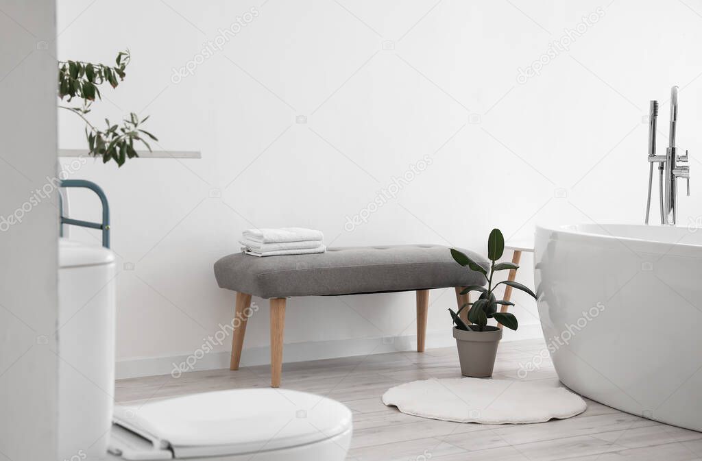 Soft bench with clean towels and houseplant near light wall in bathroom