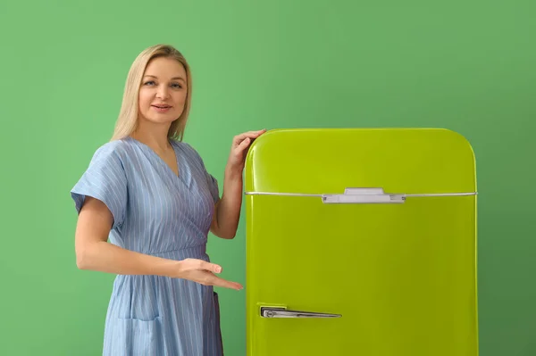 Mature woman near stylish vintage fridge on green background