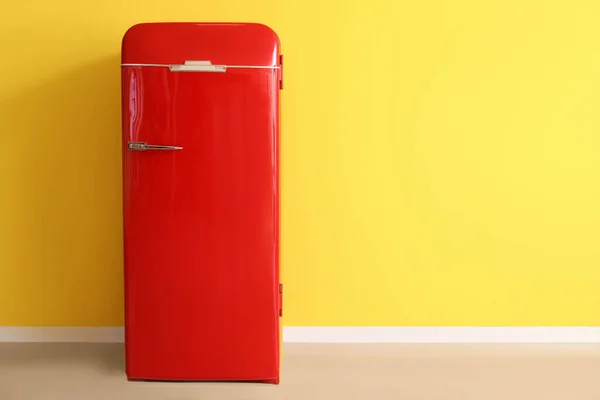 Stylish retro fridge near yellow wall in room
