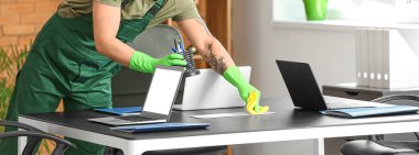 Ofisteki masadaki tozları silen erkek hademe.