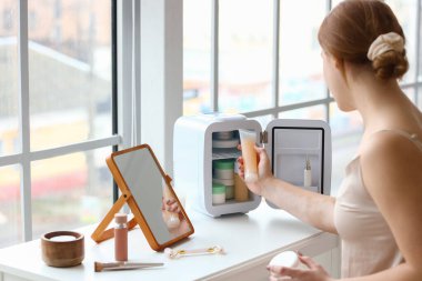 Evdeki küçük buzdolabından kozmetik ürünleri alan güzel genç bir kadın.