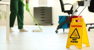 WET FLOOR işareti ve ofiste paspas ile hademe