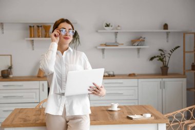 Mutfakta dizüstü bilgisayarı olan serbest çalışan genç bir kadın.