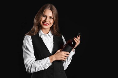 Siyah arka planda bir şişe şarabı olan güzel bir kadın şarap garsonu.