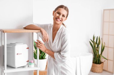 Evdeki kozmetik ürünleri için küçük buzdolabının yanında güzel bir kadın.