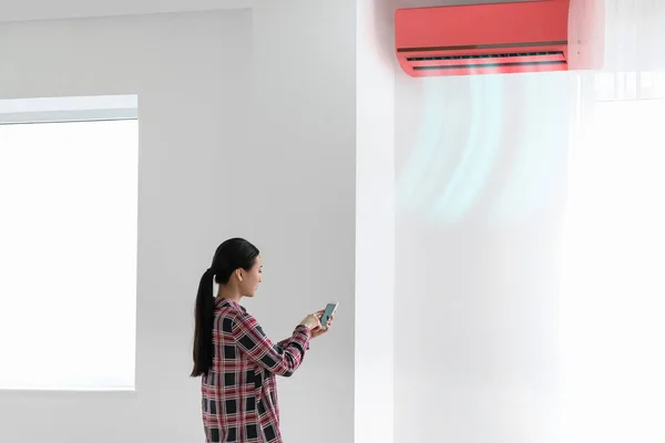 Young Asian woman with mobile phone near blowing air conditioner in room