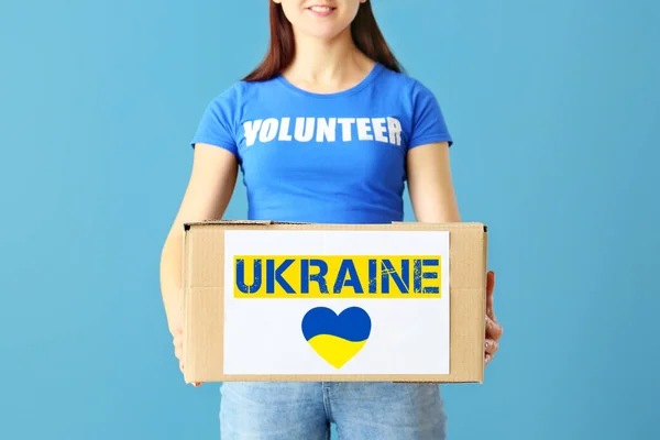 Female volunteer with donation box on blue background. Humanitarian aid for Ukraine