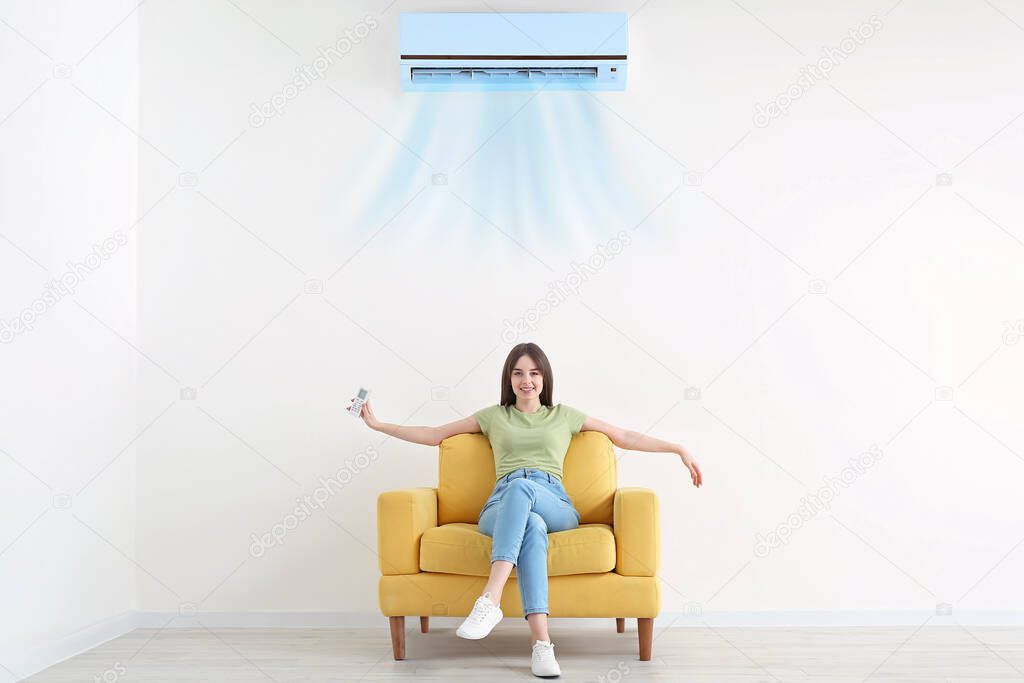 Young woman sitting in armchair near blowing air conditioner at home