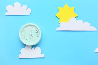 Alarm saati, kağıt bulutları ve renk arkaplanındaki güneş ile yaratıcı bileşim