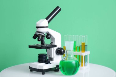 Modern mikroskop ve laboratuvar camları yeşil duvarın yanındaki masada.