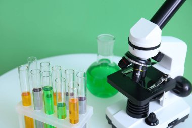 Modern mikroskop ve test tüpleri yeşil duvarın yanındaki masada, yakın plan.