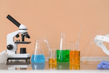 Bej duvarın yanındaki masada sıvı bulunan modern mikroskop ve laboratuvar camları.