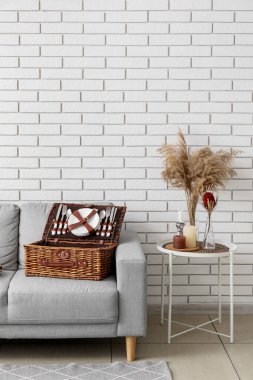 Piknik için sepetli kanepe ve beyaz tuğla duvarın yanındaki masa