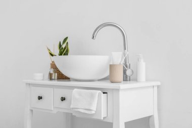 Lavabolu masa, banyo aksesuarları ve ışık duvarının yanındaki bitki örtüsü.