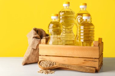 Sarı arka planda ayçiçeği tohumlarıyla dolu bir kutu dolusu yağ, torba ve kaşık.