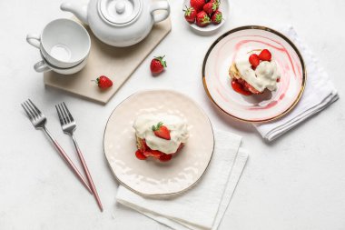 Beyaz arka planda çilekli tarçınlı, kremalı ve çaydanlıklı tabaklar