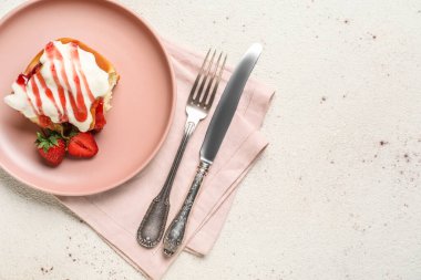 Beyaz arkaplanda çilekli tarçınlı rulo, çatal bıçak takımı ve peçete.