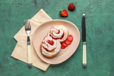 Çilekli tarçınlı tabak ve yeşil arka planda çatal bıçak takımı.