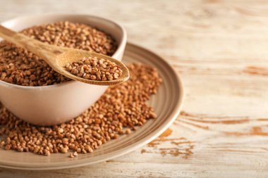 Hafif ahşap arka planda karabuğday tanecikli tabak ve kaşık, yakın plan.