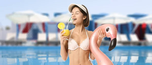Young woman with cocktail and inflatable ring in swimming pool
