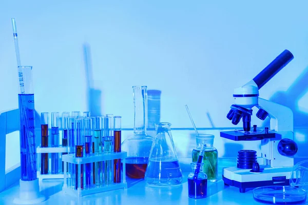 Laboratory glassware and microscope on blue background