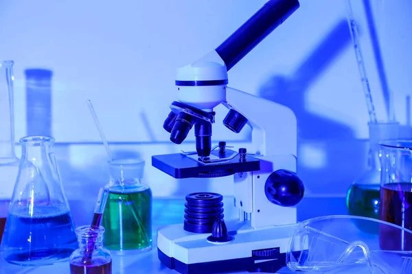 Modern microscope and laboratory glassware on blue background