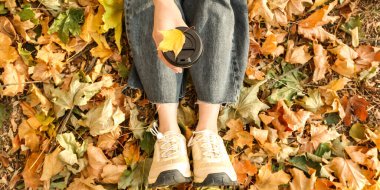 Sonbahar parkında yaprakların üzerinde oturan nefis kahveli bir kadın.