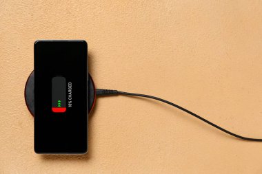 Renk arkaplanında kablosuz ped ile şarj edilen cep telefonu