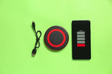 Kablosuz şarj pedi, cep telefonu ve kablo yeşil arka planda.