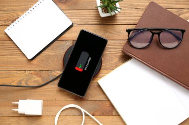 Cep telefonuna kablosuz ped ve tahta arka planda not defterleri yükleniyor.